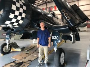 Man standing in front of a vintage navy aircraft in a hangar.