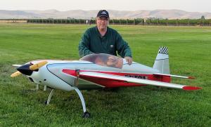 Man kneeling next to a large model airplane on grass.