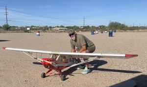 Man kneeling beside a large model airplane on a gravel surface.