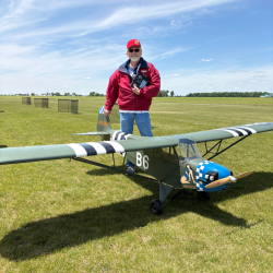 Man standing on grass field beside a large model plane.