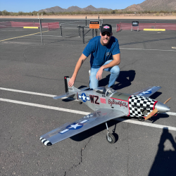 Man kneeling next to large model airplane on tarmac, sunny day.