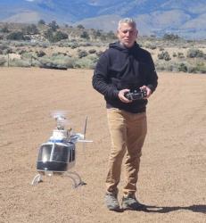 Man flying a small model helicopter outdoors on a dirt field.