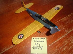 Model airplane with yellow wings on a wooden surface, note with specifications nearby.