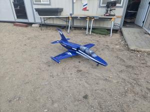 Blue and white model jet on gravel, near a building.