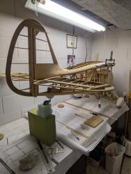 Wooden airplane model under construction in a workshop with plans and tools around.