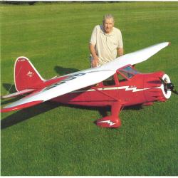 Man kneeling on grass beside a large red model airplane.