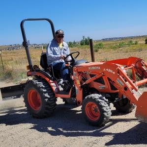 A man operates an orange tractor on a dirt path under a clear blue sky.