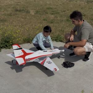 A man and child with a model jet airplane on a sunny day.