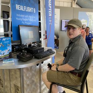 Man sitting at a demo booth with flight simulator equipment.