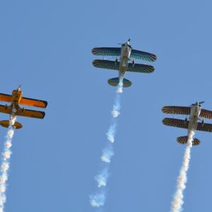 Three biplanes with colorful wings flying in formation against a clear blue sky.