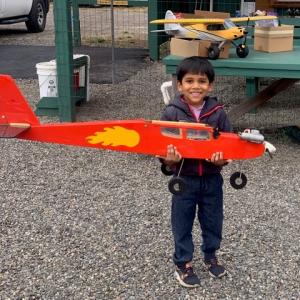 Child happily holding a red model airplane with a flame design outdoors.