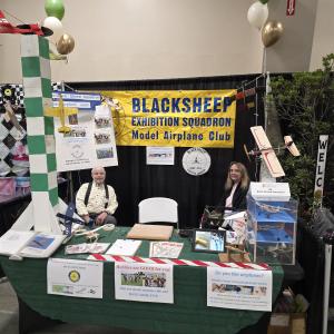 Model airplane club booth with two people, scale planes, and informational displays.