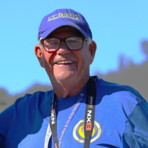 Man in blue shirt and cap, smiling outdoors under clear blue sky.