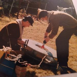 Two people working with satellite equipment outdoors on grass.