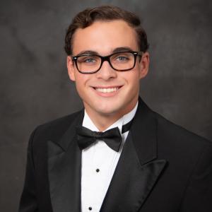 Man in a tuxedo smiling against a dark backdrop.