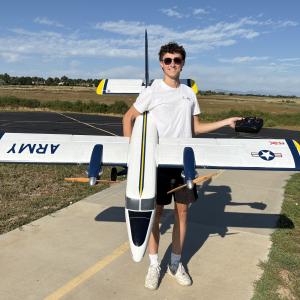 Person holding large model airplane outdoors on a sunny day.