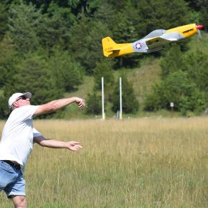 Man in field launching a yellow model airplane into the air.