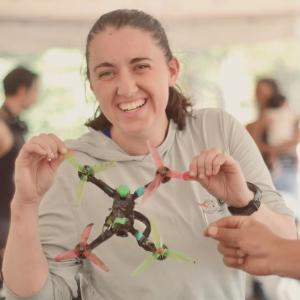 Smiling woman holding a colorful drone, surrounded by people.