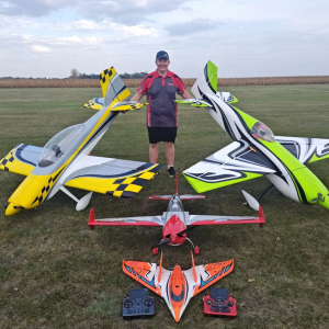 Man standing on grass with four colorful model planes arranged in front.