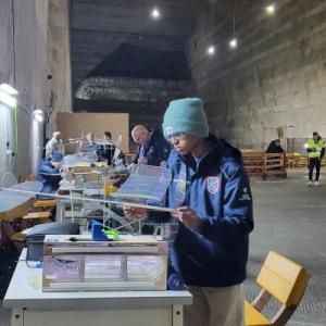 People building model airplanes in a large, dimly lit room.