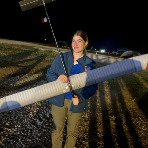 Young woman smiling, holding a model airplane at night outdoors.