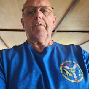 Man in a blue shirt with a logo, indoors with a wooden ceiling.