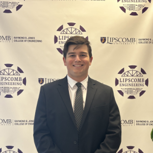 A person in a suit stands smiling in front of a Lipscomb Engineering backdrop.