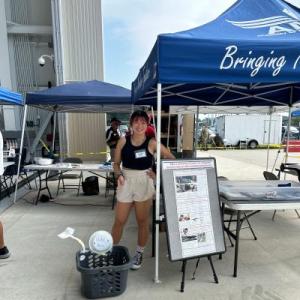 Person stands smiling under a blue tent at an outdoor event.