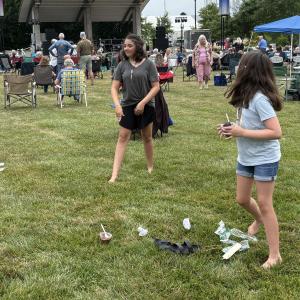 Children playing on grass at an outdoor event, surrounded by seated people.