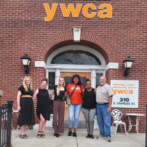 Group of six people standing in front of a brick building with "ywca" signage.