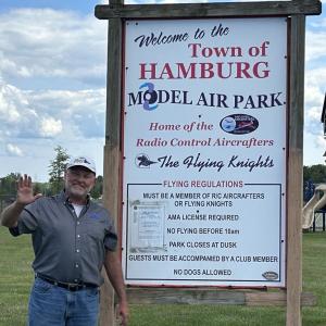 Man waving next to large sign at Hamburg Model Air Park.