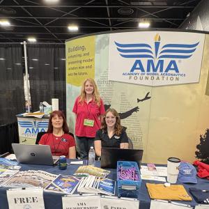 Booth with AMA Foundation banner, three people smiling, promotional items on display.