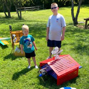 Two children stand in a sunny park with toy planes and Snoopy decoration.