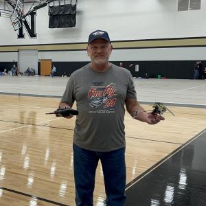 Man holding a remote and small drone in a gymnasium.