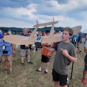 Teen holding a model airplane at an outdoor event, cloudy sky in the background.