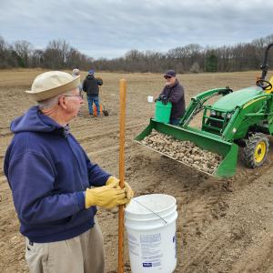 Two men planting potatoes beside a green tractor in a field.