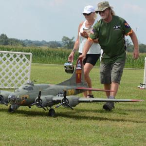 Man and woman guiding large model military plane on grass.