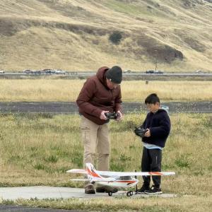 Man and boy operating a model airplane outdoors.