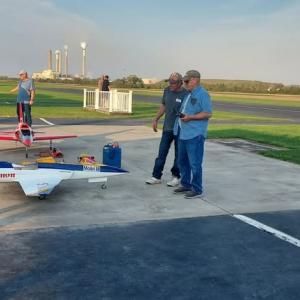 Three people preparing model airplanes on a runway under a clear sky.