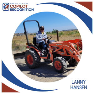 Man wearing a cap driving an orange tractor on a dirt path.