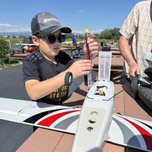 Child adjusting model airplane outdoors under clear sky.