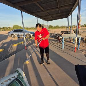 Person in a red shirt sweeping an outdoor patio in the late afternoon sun.