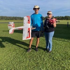 Man and woman holding model airplanes on a grassy field.