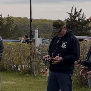Man outdoors operating a remote control, wearing a cap and hoodie.