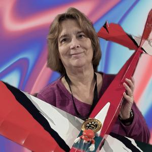 Smiling woman holding a red model plane against a colorful abstract background.