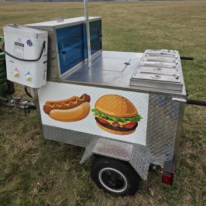 Food cart with hot dog and burger illustrations, set in a grassy field.