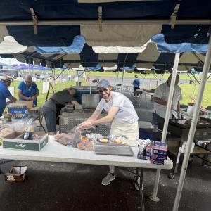 Outdoor food stall with people preparing meals under a tent.