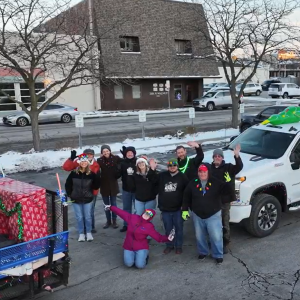 A group of people poses beside a white truck in a snowy street.