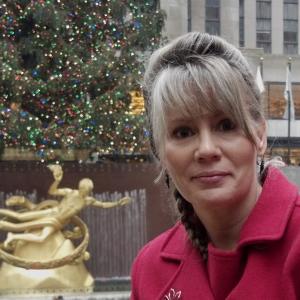 Woman in a red coat in front of a decorated Christmas tree and golden statue.