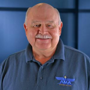 Smiling man in a blue polo with a blue background.